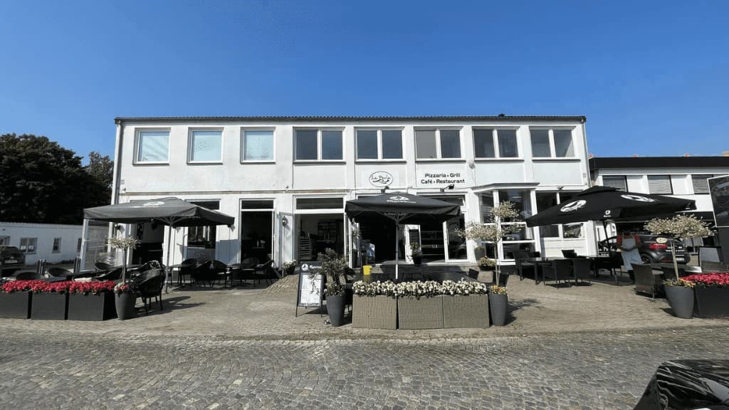 The facade of Restaurant La Perla with large black tables and umbrellas